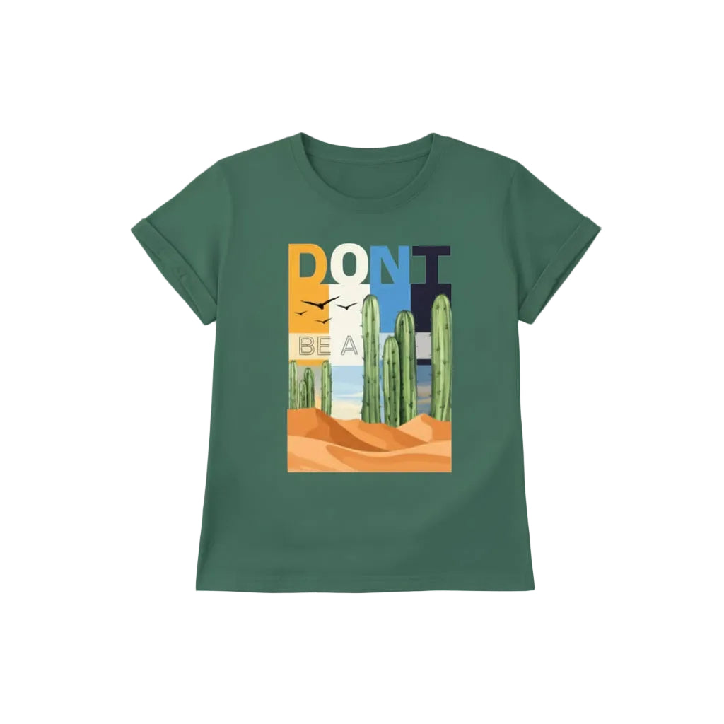 A green graphic t-shirt laid flat on a light wood background, styled with blue jeans, black canvas sneakers, sunglasses, and a leather keychain. The t-shirt features a colorful desert graphic with the text 'DON'T BE A PRICK' and illustrations of cacti and sand dunes.