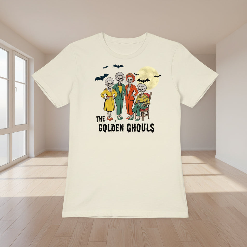 An off-white short-sleeve t-shirt featuring a colorful graphic of 'The Golden Ghouls' characters and bats, displayed against a black background with white spiderwebs.