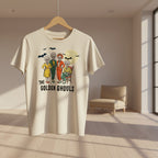 An off-white short-sleeve t-shirt featuring a colorful graphic of 'The Golden Ghouls' characters and bats, displayed against a black background with white spiderwebs.